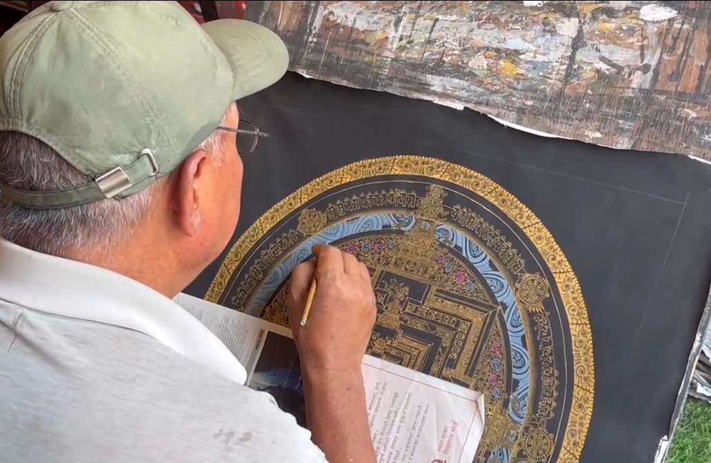 A painter adding fine detail to a circular thangka composition